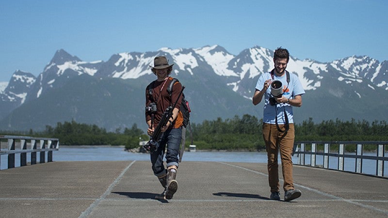 two male students with camera equipment with mountains in the background two male students with camera equipment with mountains in the background